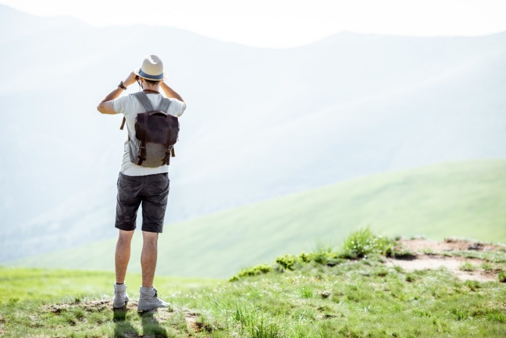 Man enjoying the beautiful views on the mountains, looking at the binoculars while traveling with backpack in the mountains during the sunny weather